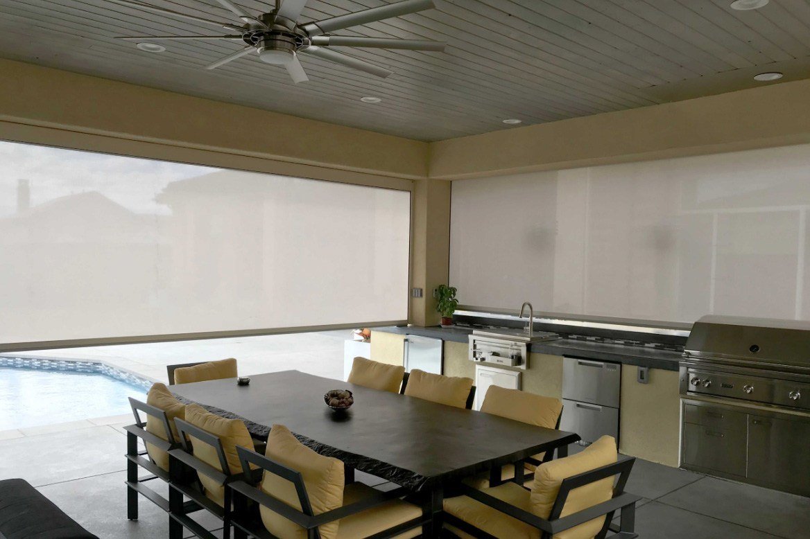 Outdoor kitchen and dining area enclosed with patio shade